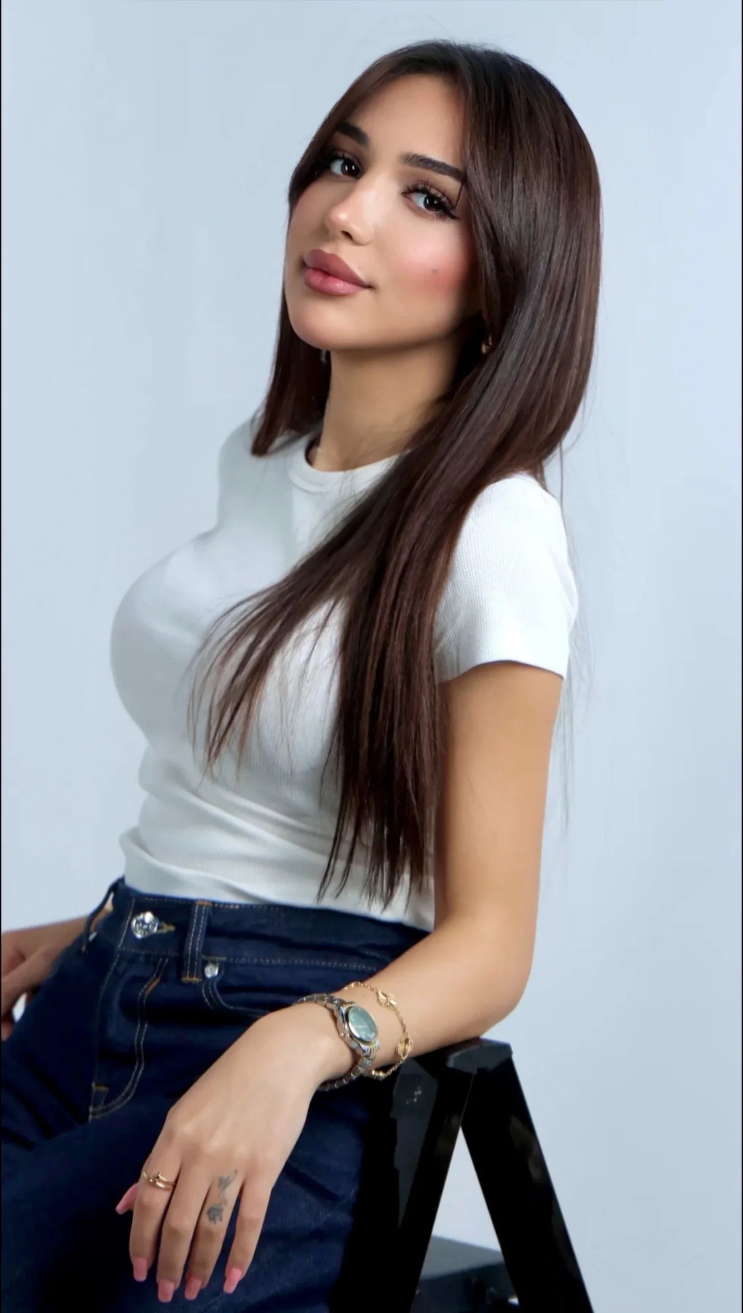 SHD, studio portrait in a white t-shirt and dark blue jeans, long dark hair, grey backdrop.