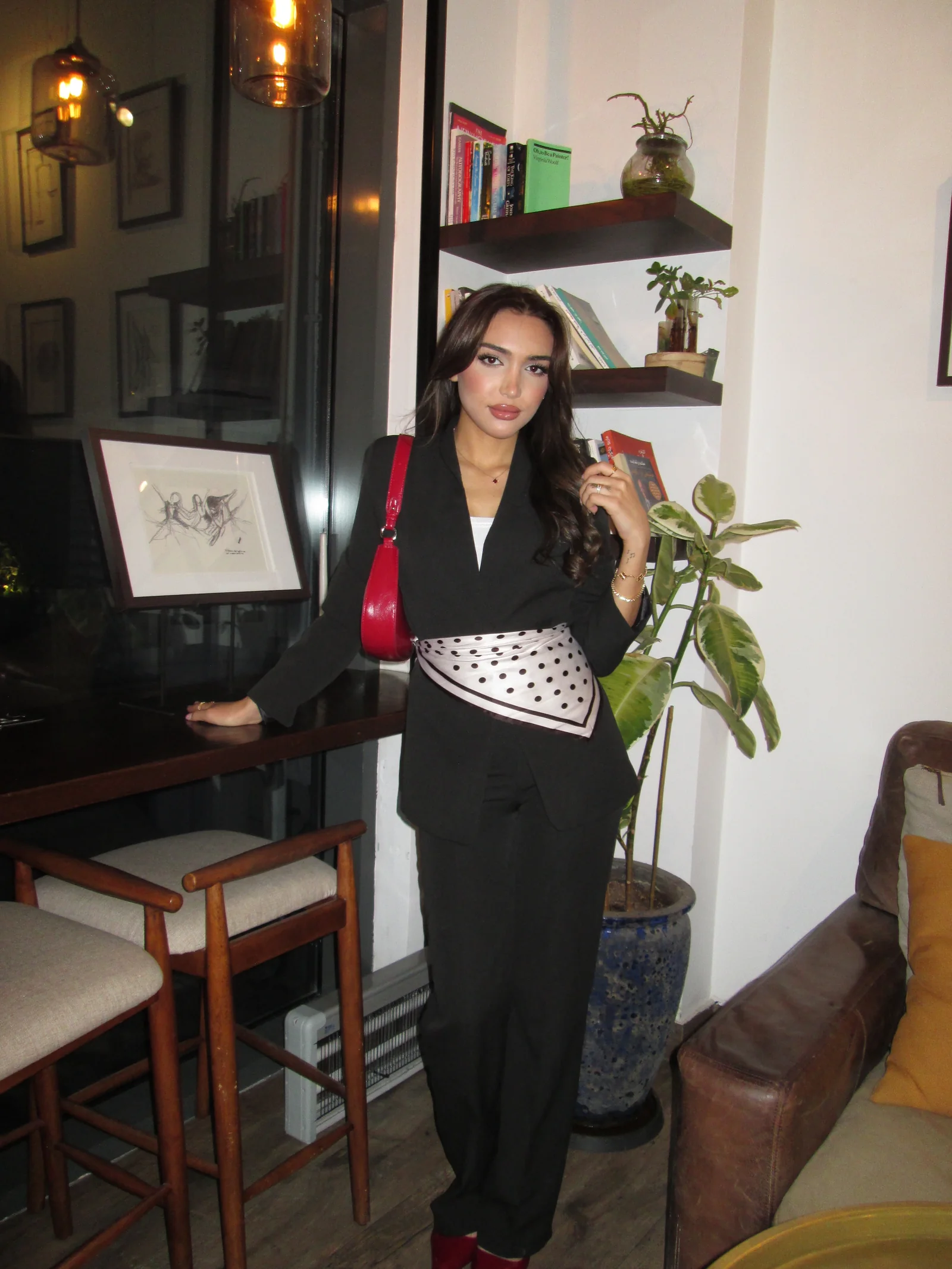 SHD in a black suit with a polka dot waist scarf and a red shoulder bag, indoor lifestyle shot.